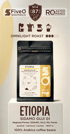 A coffee bag product display on a pedestal with branding and roast information. The main subject is a black coffee bag labeled 'ETIOPIA SIDAMO GUJI G1' with a cream and gold label.